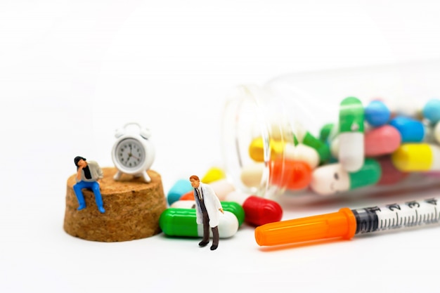 Miniature people: Patients sitting with drugs and clock. Health care concept.