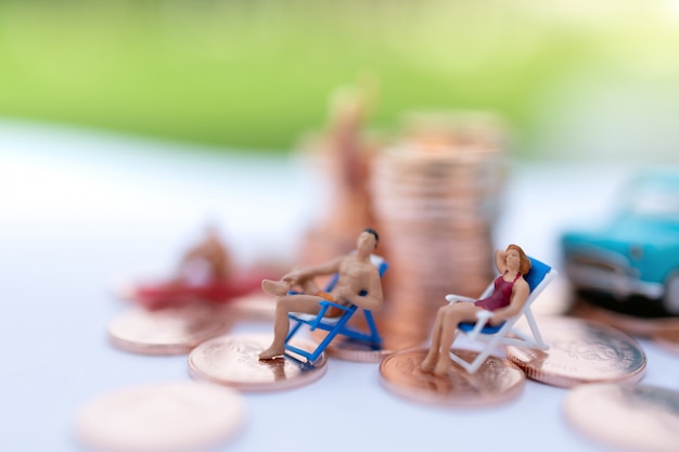 Miniature people sitting the beach with coins