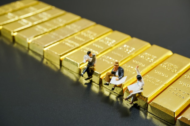 Miniature people sitting on stack of gold bar on black background