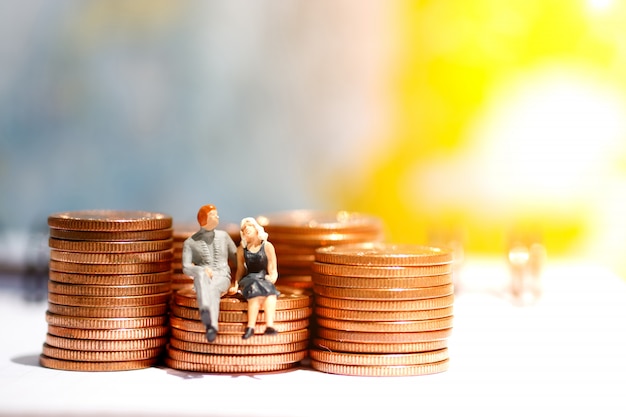 Miniature people sitting on step of coin money