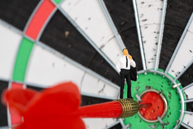 Miniature people: Small business man on red dart arrow hitting in the target center of dartboard.