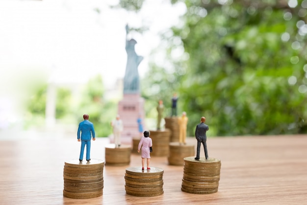 Miniature people standing on coin with statue of liberty