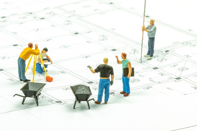 Miniature people surveyor technician is measuring the distance to build a house.