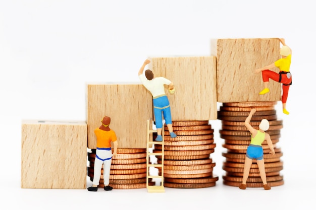 Miniature people with coins stack and wooden box.