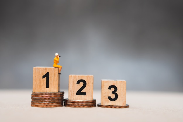 Miniature people, woman sitting on podium and stack coins 