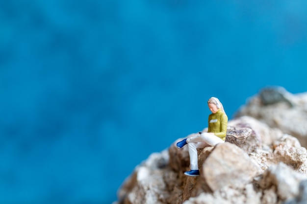 Photo miniature people woman wearing headphones and listening to music on smartphone sitting on the rock