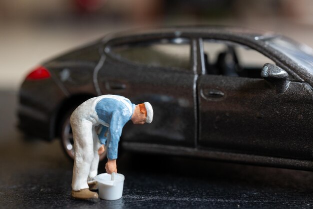 Photo miniature people a worker bends over as if inspecting or repairing something on a sleek metallic gray car model