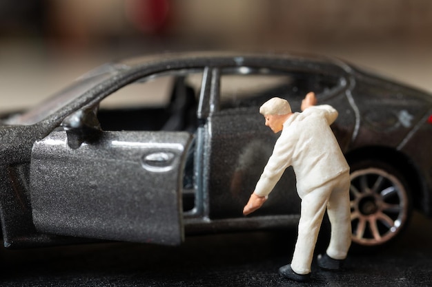 Photo miniature people a worker bends over as if inspecting or repairing something on a sleek metallic gray car model