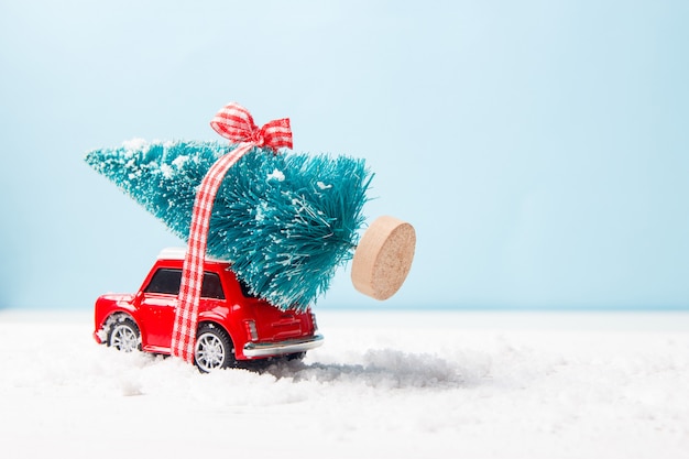 Miniature red car toy delivering christmas tree on blue