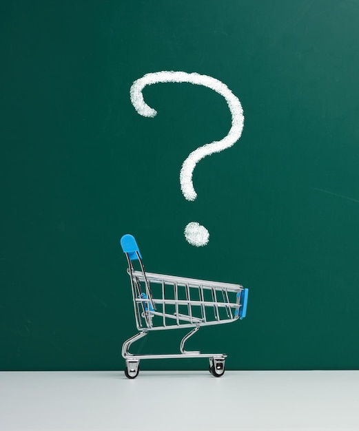 Miniature shopping cart on the background of a green board and a question mark drawn in white chalk