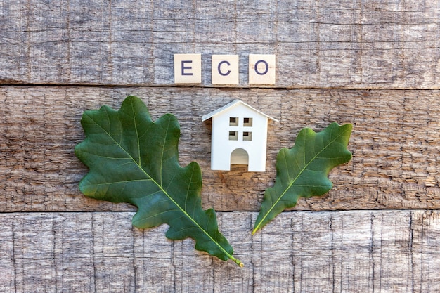 Miniature toy model house with inscription ECO letters word on wooden background