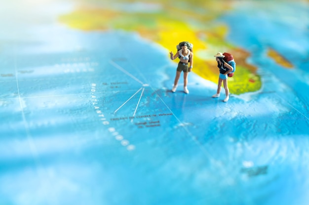 Miniature traveler with a backpack standing on world map. Travel concept.