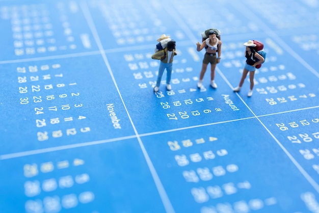 Miniature Travelers with a backpack standing on calendar, Travel and vacation Concept.