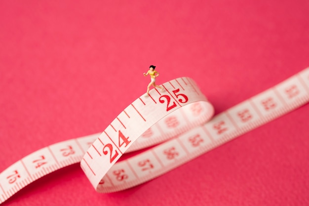 miniature woman with measure tape on pink background