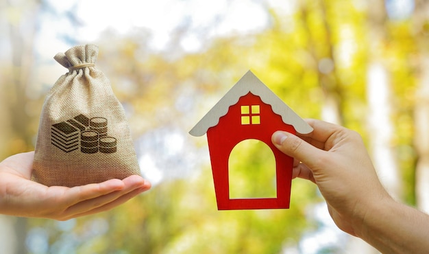 Miniature wooden house and money bag in the hands of a man outdoors Real estate concept Ecofriendly home Buying a housing outside the city Red roof Selective focus