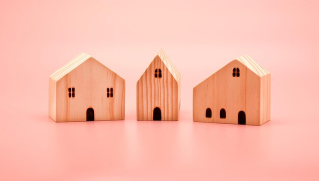 Miniature wooden houses toy isolated on pastel pink background for property and real estate concepts