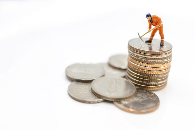 Miniature worker digging on coins stack. Concept of Money and investment.