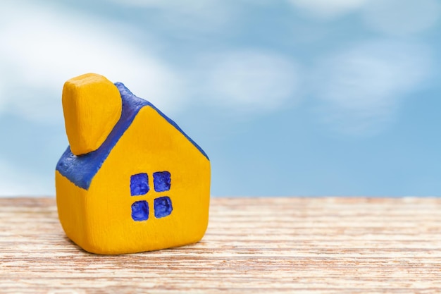 Miniature yellow toy house on wooden surface and blue background