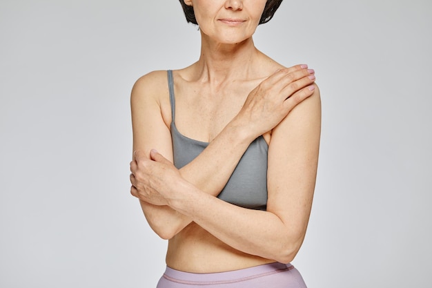 Minimal cropped shot of mature woman wearing neutral underwear against grey background covering