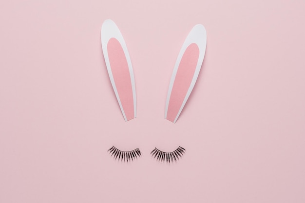 Minimal Easter concept Bunny rabbit face made of paper bunny ears with eyelashes on pastel pink background Flat lay