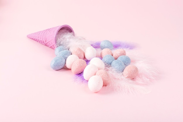 Minimal Easter concept Ice cream cone with pastel color eggs on feathers on pink background Copy space