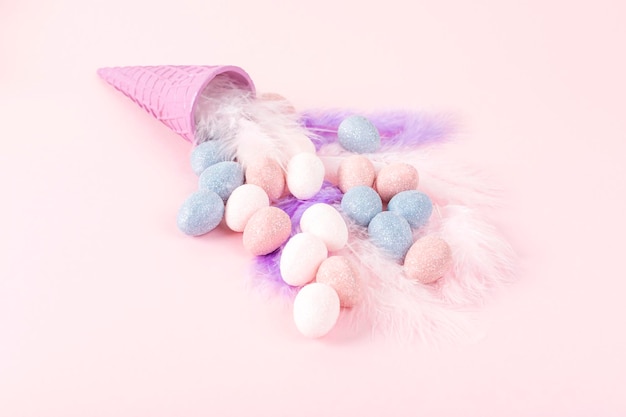 Minimal Easter concept Ice cream cone with pastel color eggs on feathers on pink background Copy space