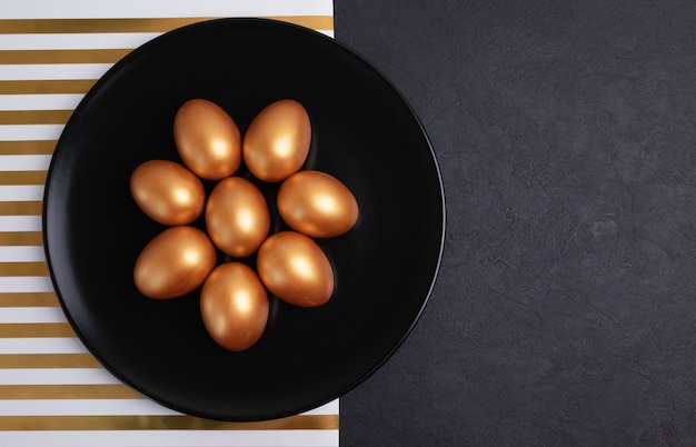 Minimal easter concept. Stylish Easter golden decorated eggs on black plate isolated on black marble background