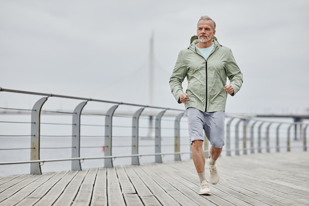 Minimal full length portrait of handsome mature man running towards camera outdoors by river copy sp