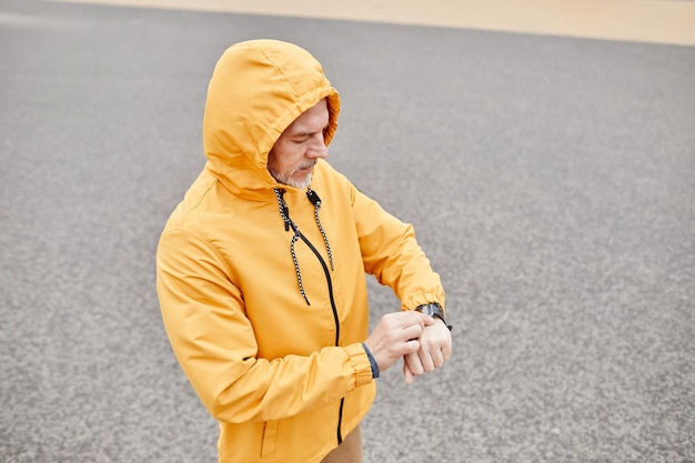 Minimal high angle portrait of mature man checking fitness watch while enjoying running outdoors in