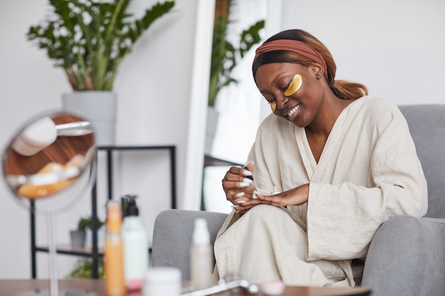 Minimal portrait of beautiful African-American woman enjoying skincare routine at home and doing manicure, copy space