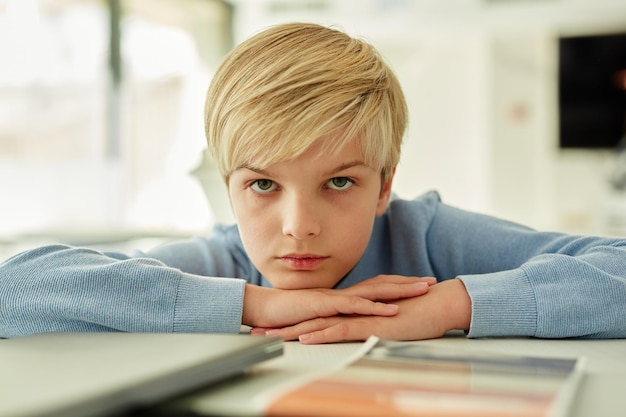 Photo minimal portrait of bored schoolboy lying on desk in school classroom and looking away