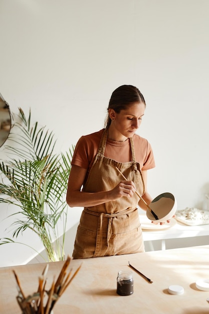 Minimal portrait of young female artist decorating ceramics in pottery workshop copy space