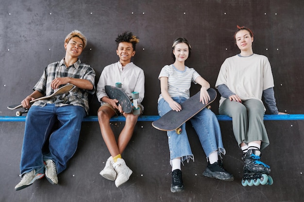 Minimal shot of diverse group of teenagers looking at camera while sitting on ramp in skateboarding