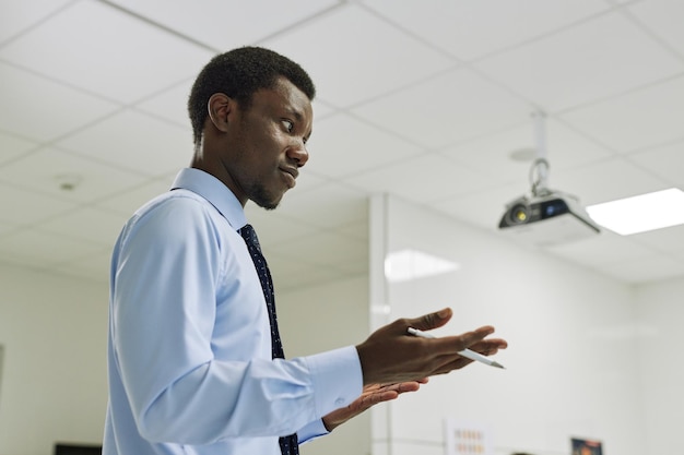 Minimal side view portrait of young black teacher giving lecture in class and gesturing copy space