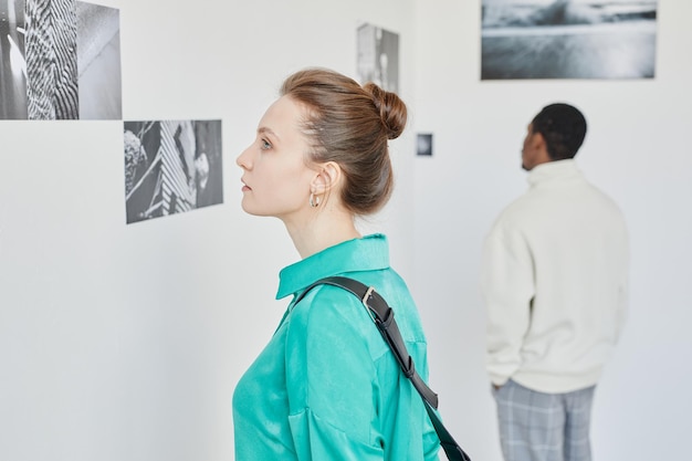 Minimal side view portrait of young woman looking at photography in art gallery copy space