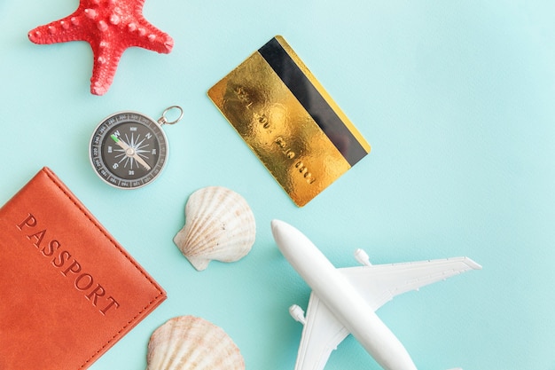 Minimal simple flat lay with plane passport compass gold credit card and shell on blue pastel. Tourist essentials