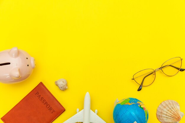 Minimal simple flat lay with plane passport sunglasses globe piggy bank and shell on yellow colourful trendy. Tourist essentials