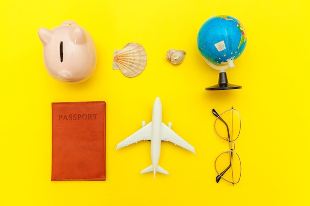 Minimal simple flat lay with plane passport sunglasses globe piggy bank sleeping eye mask and shell on yellow colourful trendy