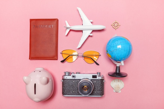 Minimal simple flat lay with plane vintage camera passport sunglasses globe piggy bank and shell on pink pastel trendy modern