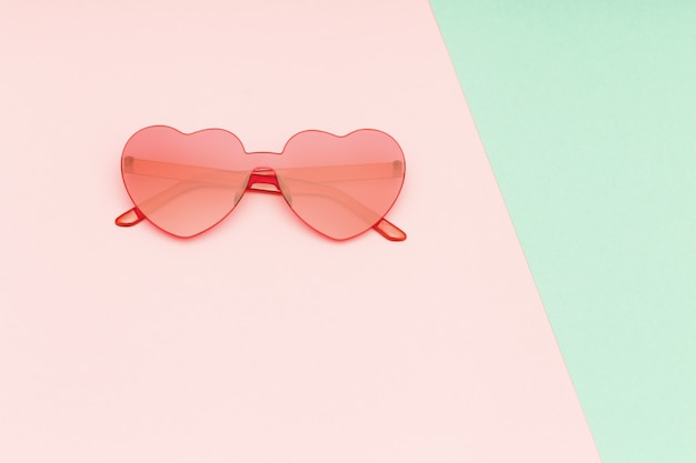 Minimal style fashion photography with heart shaped glasses on green and pink paper background. Modern sunglasses. Trendly summer concept. Copy space.