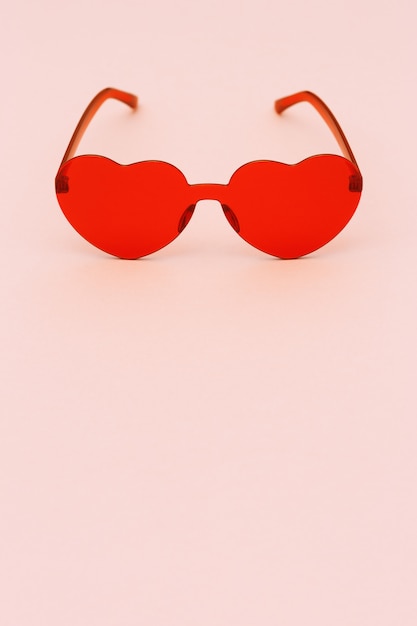 Minimal style fashion photography with heart shaped glasses on paper background. Red modern sunglasses.  Trendly summer concept. Copy space.