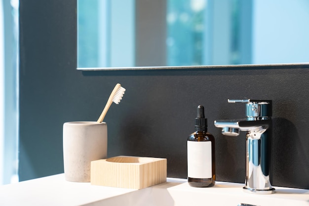 Minimal toiletries such as toothbrush serum bottle and wood storage on white sink and mirror on the black wall