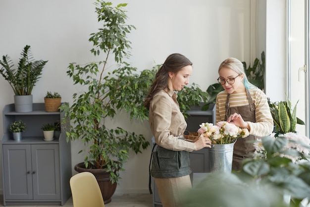 Minimal wide angle portrait of two young women arranging bouquets while enjoying work in florists studio, copy space