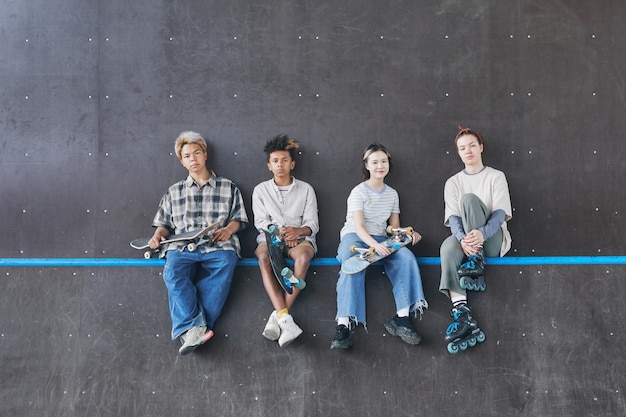 Minimal wide angle shot of diverse group of teenagers sitting on ramp in skateboarding park and look