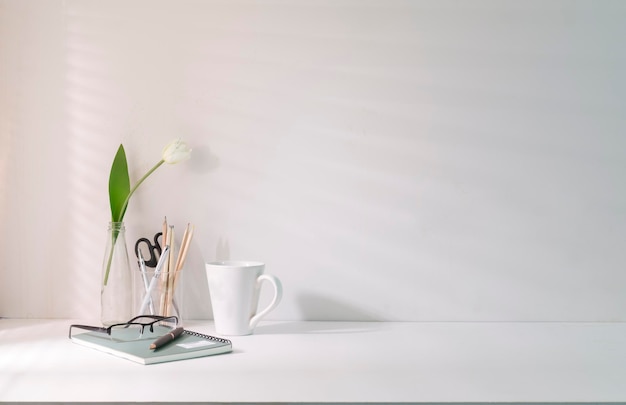 Minimal workplace with coffee cup pencil holder notebook and flower pot on white table Copy space for your advertise text