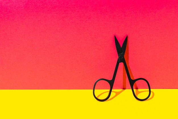 Photo minimalist black scissors on vibrant pink and yellow background conceptual art design