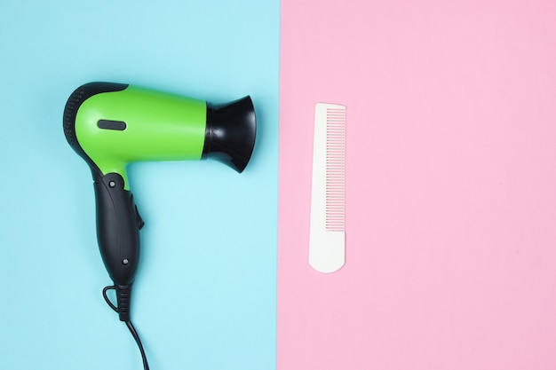 Minimalistic beauty and fashion still life. Hair dryer and comb on blue pink.