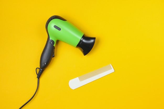 Minimalistic beauty and fashion still life. Hair dryer and comb on yellow.