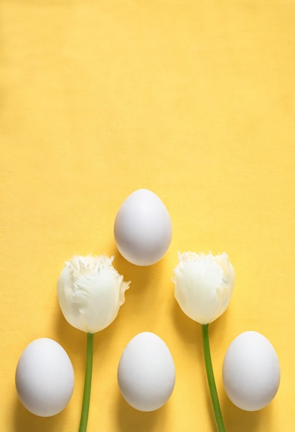 Minimalistic Easter flat lay with Easter eggs and white tulips on a yellow background