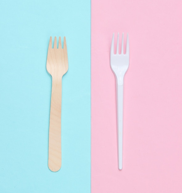 Minimalistic environmental concept. Wooden and plastic forks on a pink blue pastel background. Creative eco background